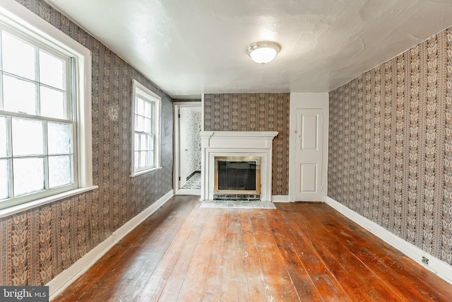 unfurnished living room with wallpapered walls, a fireplace with flush hearth, baseboards, and wood-type flooring