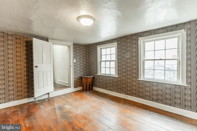 empty room featuring wallpapered walls and hardwood / wood-style flooring