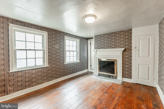 unfurnished living room featuring a fireplace with flush hearth, baseboards, hardwood / wood-style floors, and wallpapered walls