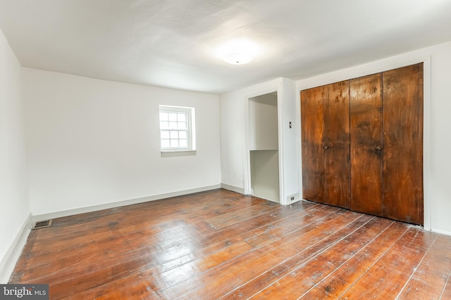 unfurnished bedroom featuring hardwood / wood-style flooring, baseboards, visible vents, and a closet