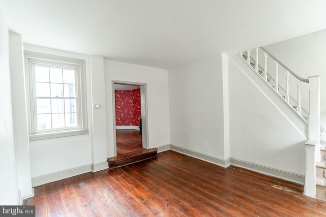 unfurnished living room featuring wood-type flooring, stairs, and baseboards