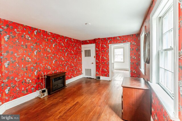 unfurnished living room with baseboards, wood finished floors, and wallpapered walls