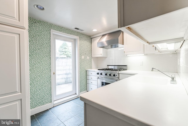 kitchen with wallpapered walls, visible vents, stainless steel range, wall chimney range hood, and a sink