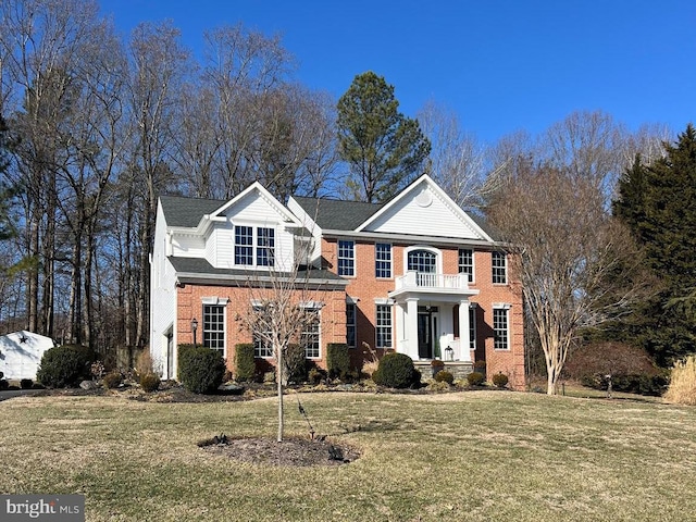 colonial home featuring brick siding, a front yard, and a balcony