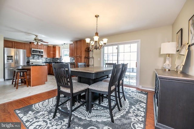 dining space with ceiling fan with notable chandelier, light wood-type flooring, and baseboards