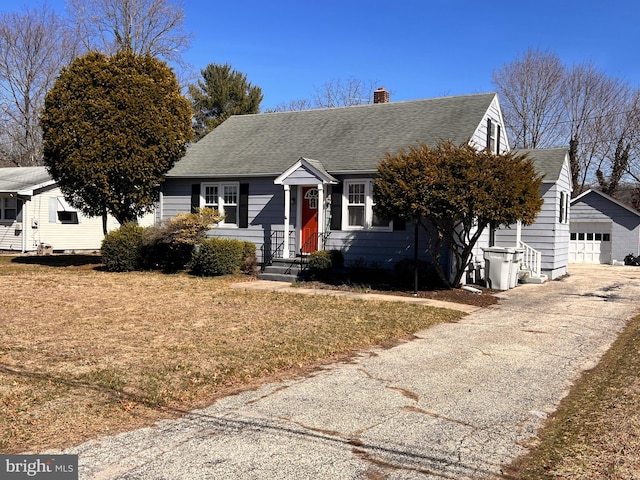 view of front of home with driveway, a chimney, a shingled roof, an outdoor structure, and a garage