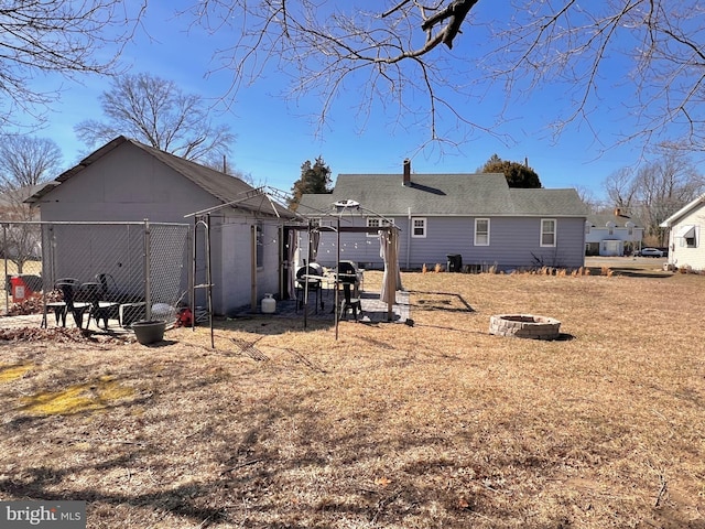 rear view of property featuring a fire pit, roof with shingles, and fence