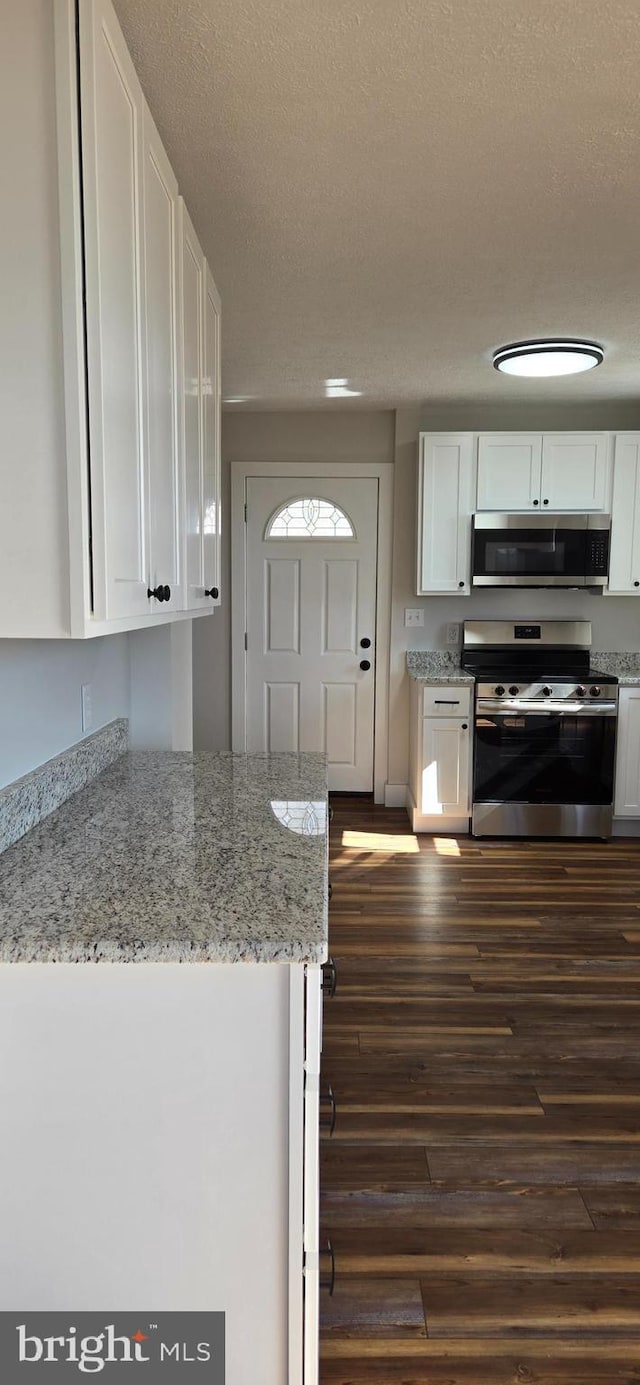 kitchen featuring light stone countertops, stainless steel appliances, dark wood-style floors, white cabinets, and a textured ceiling