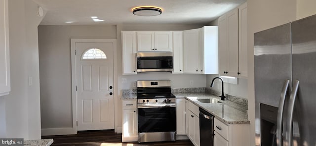 kitchen featuring white cabinets, appliances with stainless steel finishes, light stone countertops, and a sink