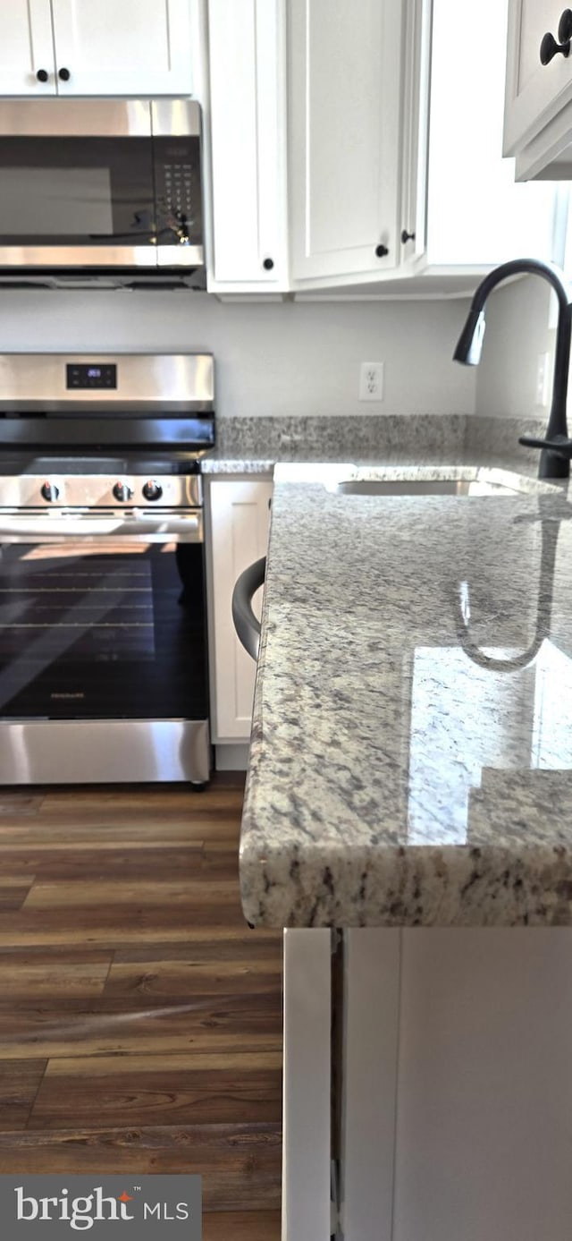 kitchen featuring light stone countertops, a sink, dark wood-type flooring, white cabinets, and appliances with stainless steel finishes