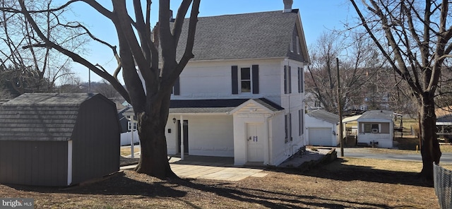 view of home's exterior with a shingled roof, a detached garage, concrete driveway, a storage shed, and an outbuilding