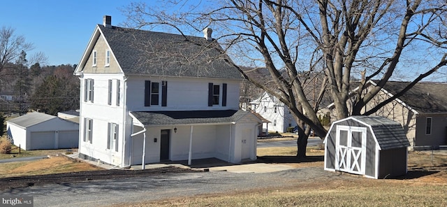 view of front of property with a detached garage, an outbuilding, a shed, and a shingled roof