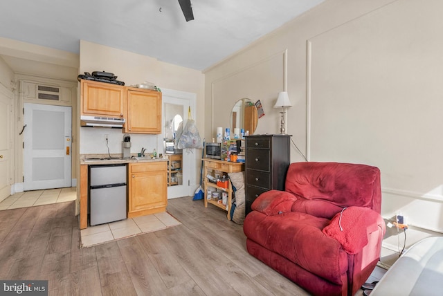 kitchen featuring under cabinet range hood, a sink, refrigerator, light wood-style floors, and light countertops