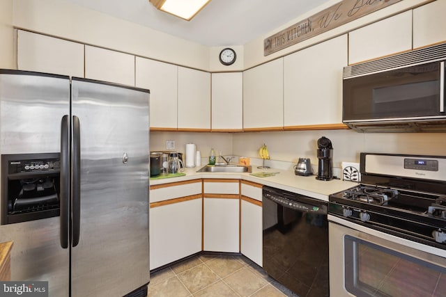 kitchen with light countertops, light tile patterned flooring, white cabinets, black appliances, and a sink