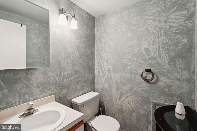 half bath with wallpapered walls, toilet, and vanity