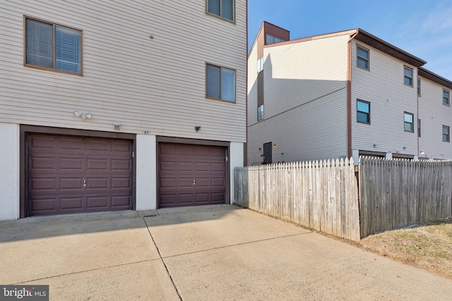 view of side of property featuring an attached garage, concrete driveway, and fence