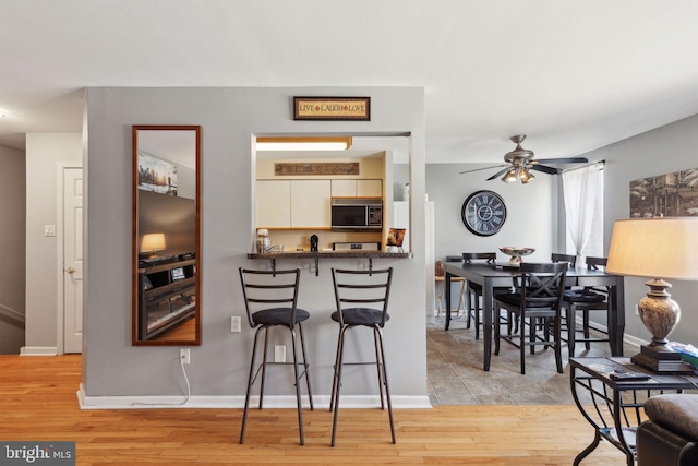 kitchen featuring a kitchen bar, dark countertops, light wood-type flooring, and a ceiling fan