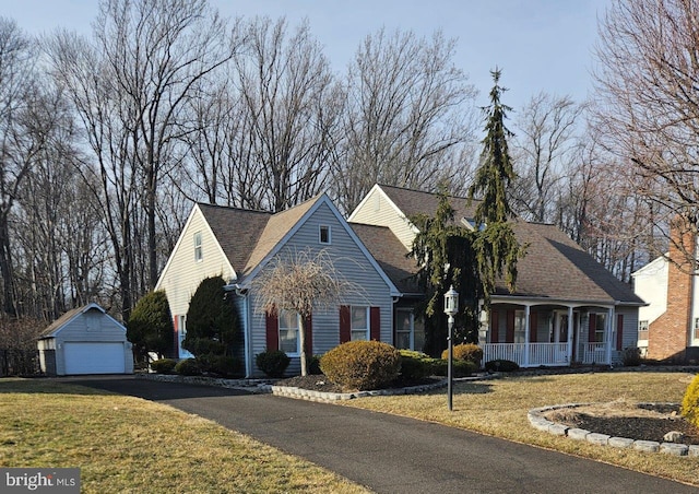 view of front facade with a shingled roof, a detached garage, a front yard, covered porch, and an outbuilding