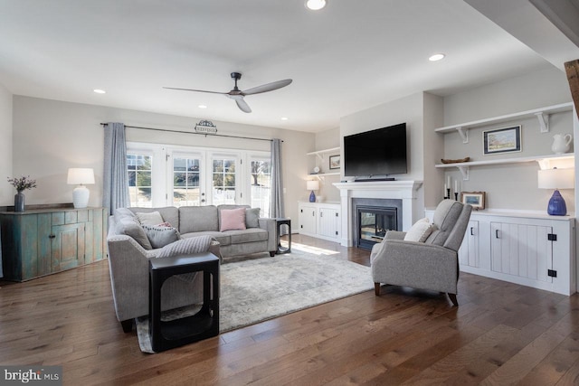 living room featuring ceiling fan, dark wood-type flooring, and a glass covered fireplace