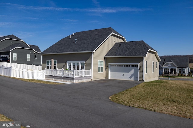 ranch-style house featuring an attached garage, fence, driveway, roof with shingles, and a front lawn