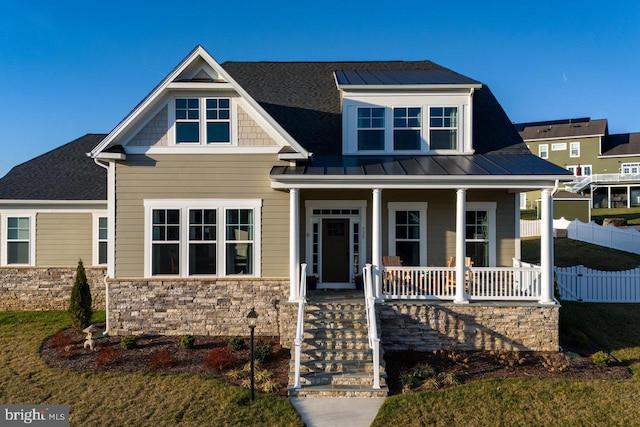 craftsman-style house featuring stone siding, metal roof, covered porch, a standing seam roof, and fence