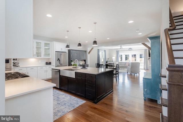 kitchen with glass insert cabinets, appliances with stainless steel finishes, open floor plan, light countertops, and a sink