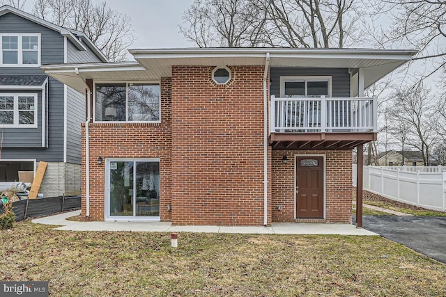 view of front of property featuring a balcony, a front yard, fence, and brick siding