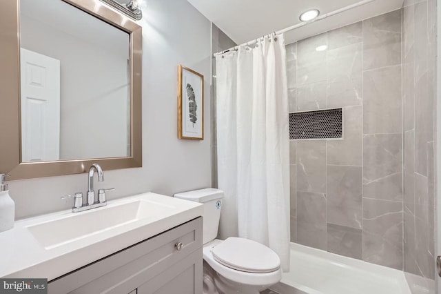 full bathroom featuring toilet, tiled shower, and vanity