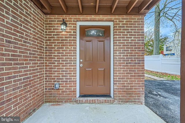 doorway to property featuring fence and brick siding