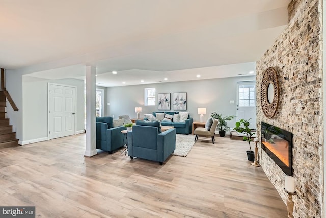 living room with a large fireplace, stairs, a wealth of natural light, and light wood-style floors