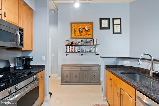 kitchen with brown cabinetry, dark stone counters, light wood-style flooring, stainless steel appliances, and a sink