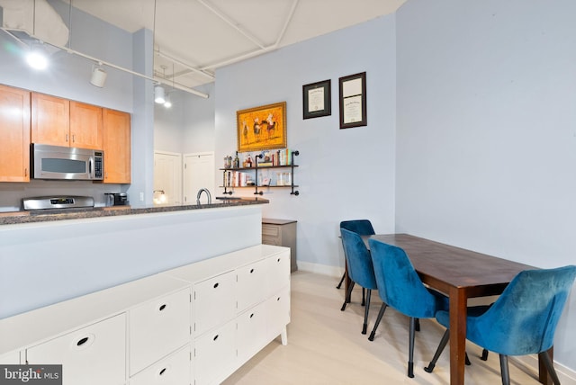 kitchen featuring dark countertops, rail lighting, stainless steel microwave, a towering ceiling, and baseboards