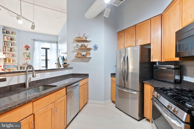 kitchen with open shelves, stainless steel appliances, a sink, track lighting, and dark stone counters