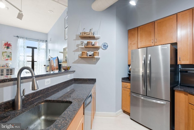 kitchen featuring dishwashing machine, a sink, freestanding refrigerator, brown cabinets, and dark stone countertops