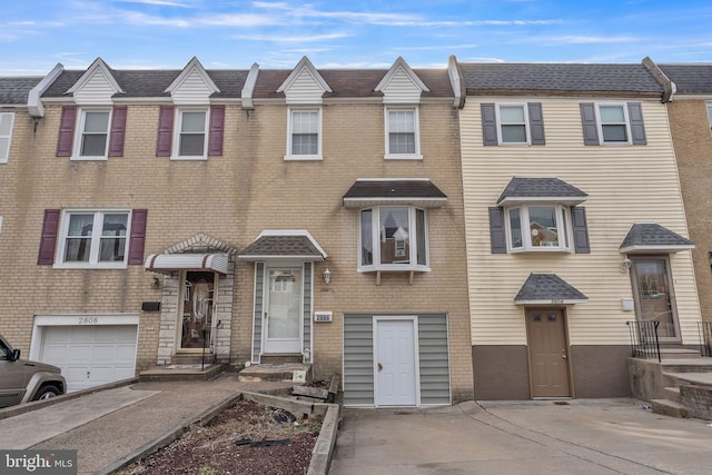 townhome / multi-family property with driveway, a shingled roof, and brick siding