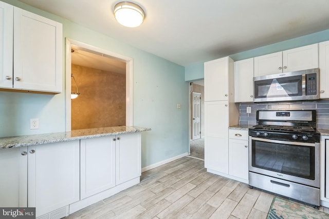 kitchen with decorative backsplash, appliances with stainless steel finishes, light wood-style floors, white cabinets, and light stone countertops