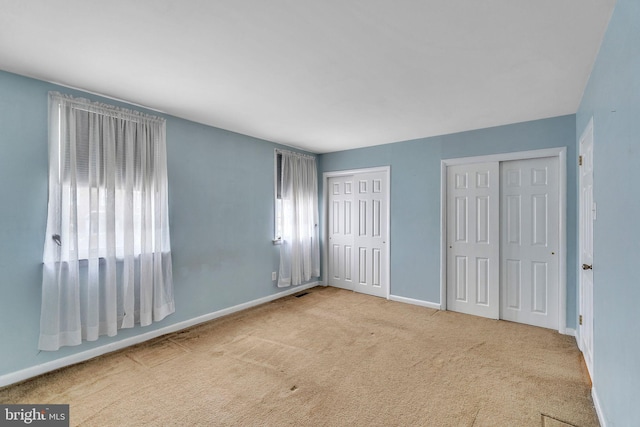 unfurnished bedroom featuring carpet floors, baseboards, and two closets