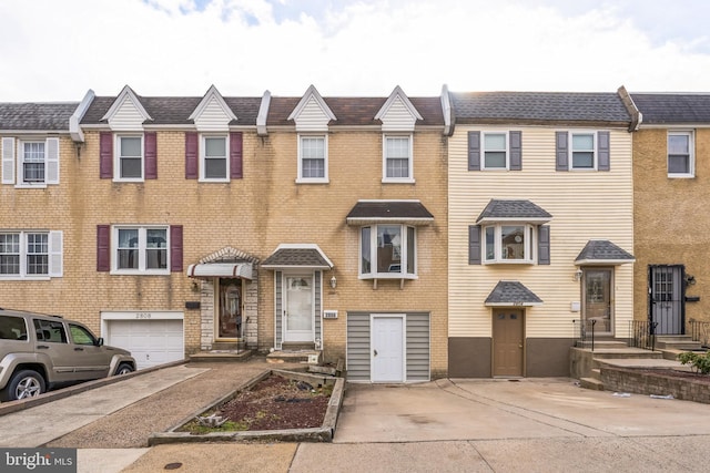 townhome / multi-family property with a garage, driveway, and brick siding