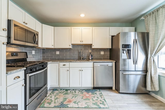 kitchen with white cabinets, light stone counters, a sink, stainless steel appliances, and backsplash