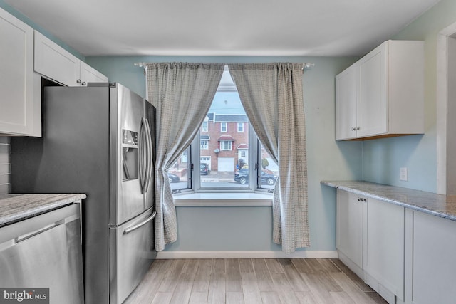 kitchen with light stone counters, stainless steel appliances, light wood-style flooring, white cabinetry, and baseboards