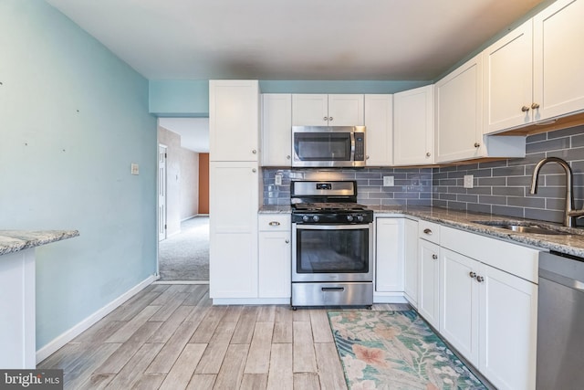 kitchen with stainless steel appliances, decorative backsplash, light wood-style floors, white cabinetry, and a sink