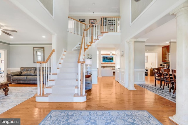 foyer entrance featuring hardwood / wood-style floors, crown molding, a ceiling fan, and ornate columns