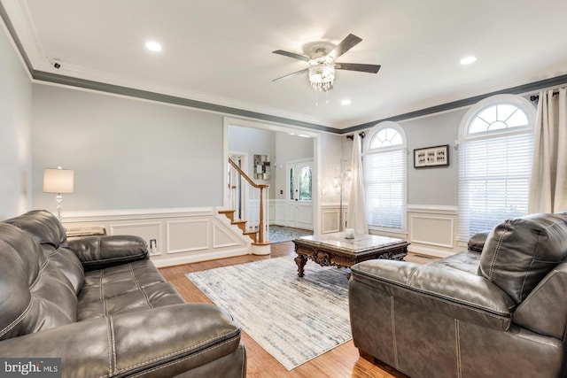 living room with ceiling fan, stairs, ornamental molding, light wood-style floors, and wainscoting