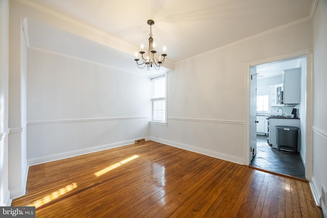 spare room featuring visible vents, baseboards, ornamental molding, hardwood / wood-style flooring, and a notable chandelier