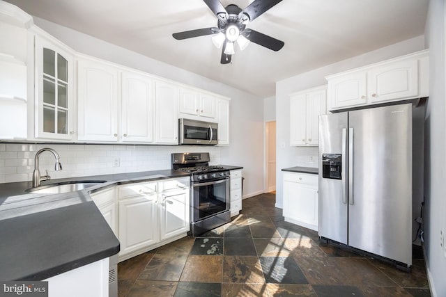 kitchen with a sink, dark countertops, appliances with stainless steel finishes, and stone finish floor