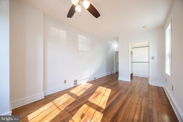 unfurnished bedroom featuring visible vents, a walk in closet, a ceiling fan, hardwood / wood-style flooring, and baseboards