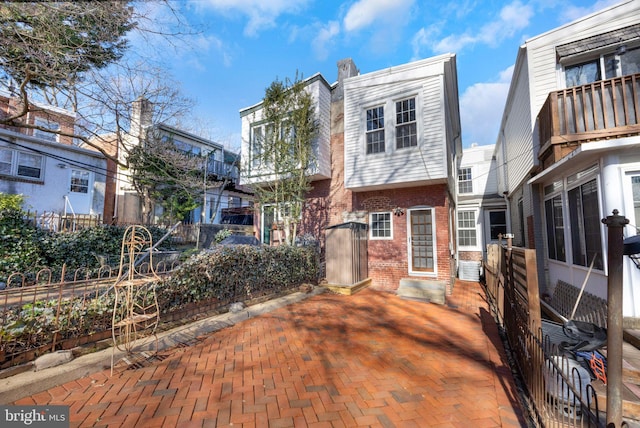 rear view of house with entry steps, a patio, fence, and brick siding