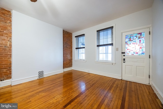 foyer with visible vents, baseboards, brick wall, and hardwood / wood-style flooring