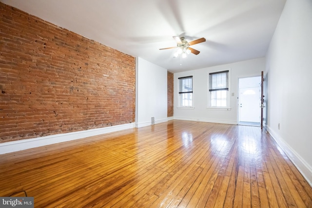 spare room featuring hardwood / wood-style flooring, baseboards, brick wall, and ceiling fan