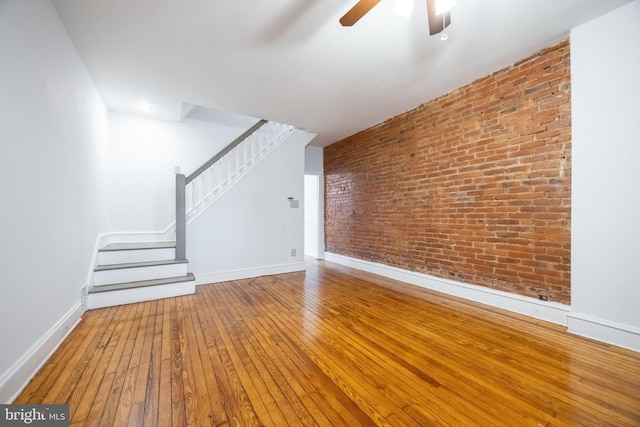 unfurnished living room with stairs, brick wall, baseboards, and hardwood / wood-style floors